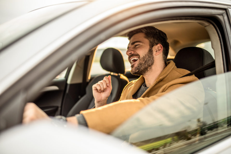 adult man driving a car and singing.